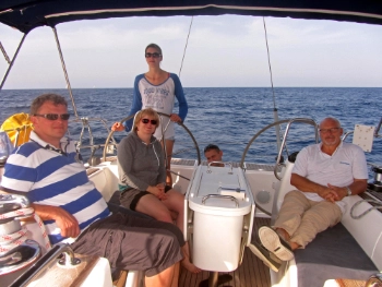 5 Personen im Cockpit eines Segelbootes, im Hintergrund blaues Wasser